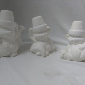 May include: Three white ceramic squirrel figurines with hats. The squirrels are sitting and have their tails curled up behind them.