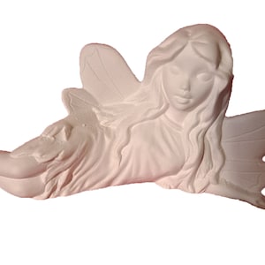 May include: White ceramic fairy figurine with wings, lying on its side with its head resting on its hand. The fairy has long hair and a delicate face.