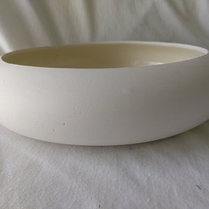 May include: A smooth, off-white ceramic bowl with a rounded shape. The interior is a lighter cream color. The bowl is designed with a wide opening and a shallow depth, suitable for decorative or functional use.