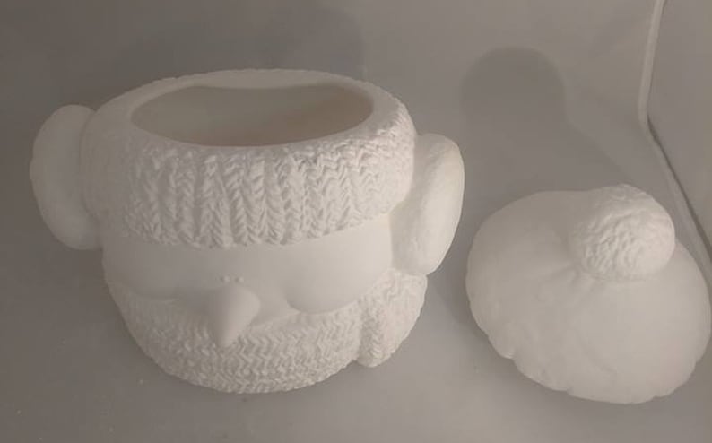 Op de afbeelding: Witte keramische sneeuwman koekjespot met een gebreide muts en een afneembaar deksel. De pot is leeg en klaar om te beschilderen.