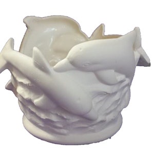 May include: White ceramic planter shaped like three dolphins jumping out of the water. The planter is a great way to add a touch of whimsy to your home decor.