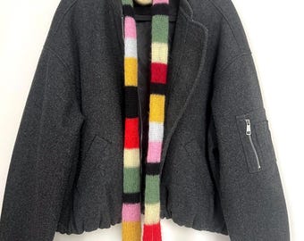 May include: A charcoal grey bomber jacket with a multi-coloured striped scarf. The scarf features vertical stripes of yellow, pink, green, red, and black. The jacket has a zip pocket on the left sleeve and a zip closure.
