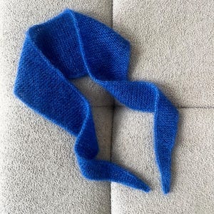May include: A vibrant blue knitted scarf, displayed on a neutral gray surface. The scarf is made of a soft, textured material and is draped in a flowing, elegant design. The scarf's color is a rich, saturated blue.