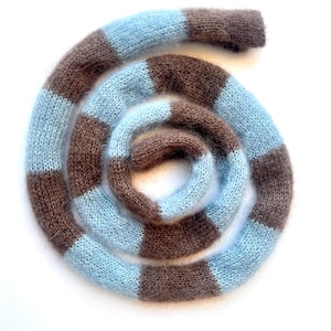 Peut inclure: Une écharpe enroulée, composée de bandes alternées bleu clair et marron. Le tissu est doux et duveteux, offrant une texture agréable. Le motif à blocs de couleurs crée un effet visuel intéressant et chaleureux.