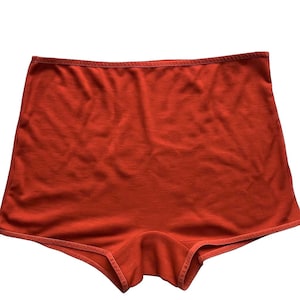 May include: A pair of orange shorts with a high waist and a simple design. The shorts are made of a soft, textured fabric and have a contrasting trim around the edges. The garment is displayed against a white background.