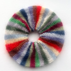 May include: A colorful, striped scrunchie in a circular shape. The scrunchie features a variety of colors, including red, green, blue, and purple. The material appears to be soft and fuzzy, with a knitted or woven texture. This hair accessory is perfect for adding a pop of color to any hairstyle.