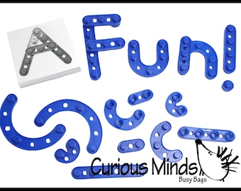 May include: Blue plastic building blocks spelling "FUN!" and other shapes. A gray letter "A" is assembled on a white card. The words "Curious Minds Busy Bags" are also visible.