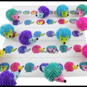 May include: A set of colorful spiky hedgehog toys with smiling faces. The hedgehogs are arranged in rows on a white background with printed hedgehogs.