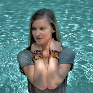 May include: A woman wearing a gray shirt with colorful bracelets on both wrists. The bracelets are made of beads and have a variety of shapes and colors.
