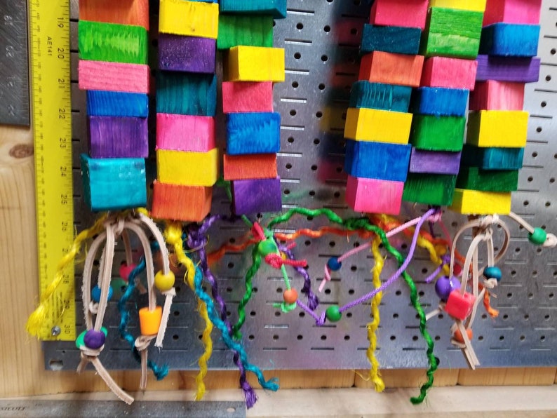 May include: Two colorful wooden toy bird perches with multi-colored wooden blocks and leather straps with colorful strings and beads.