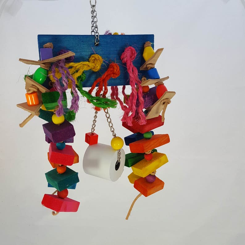 Op de afbeelding: Een kleurrijk vogelspeelgoed met een blauwe houten basis, een verscheidenheid aan houten blokken, kralen en touwen, en een witte papieren rol die aan een ketting hangt.
