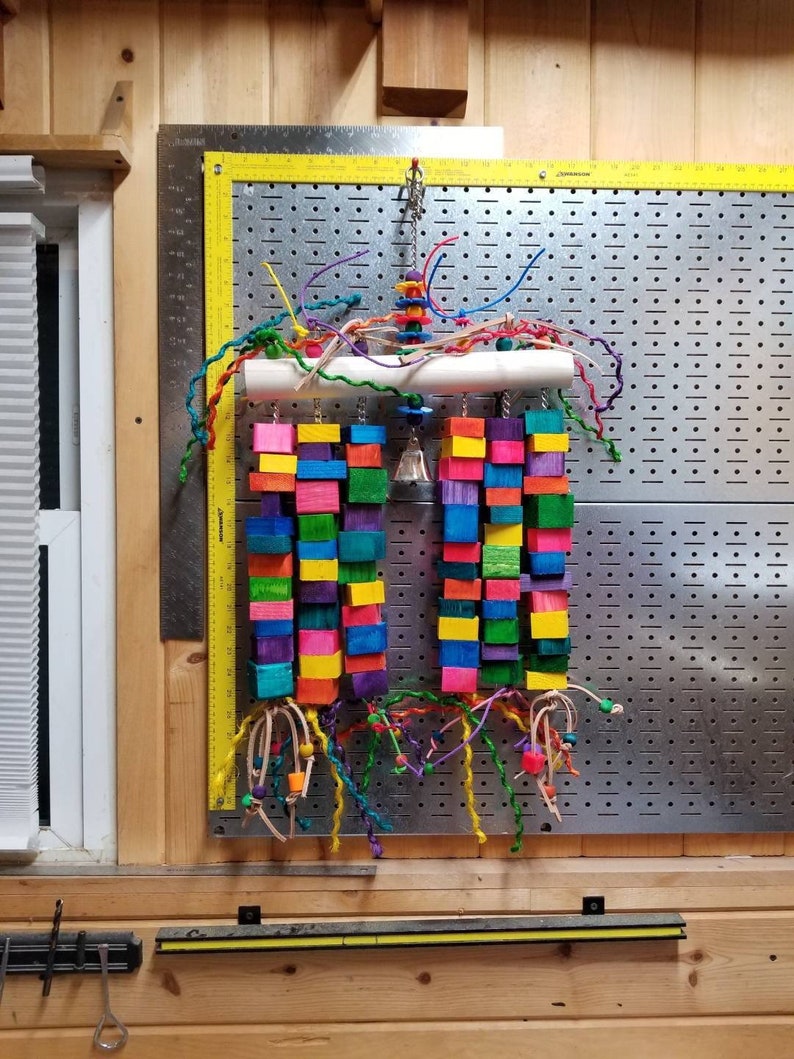 May include: A colorful wooden bird toy with a variety of textures and shapes. The toy is made up of small wooden blocks in various colors, including red, blue, green, yellow, and purple. The toy also includes a bell and a variety of colorful strings and beads.