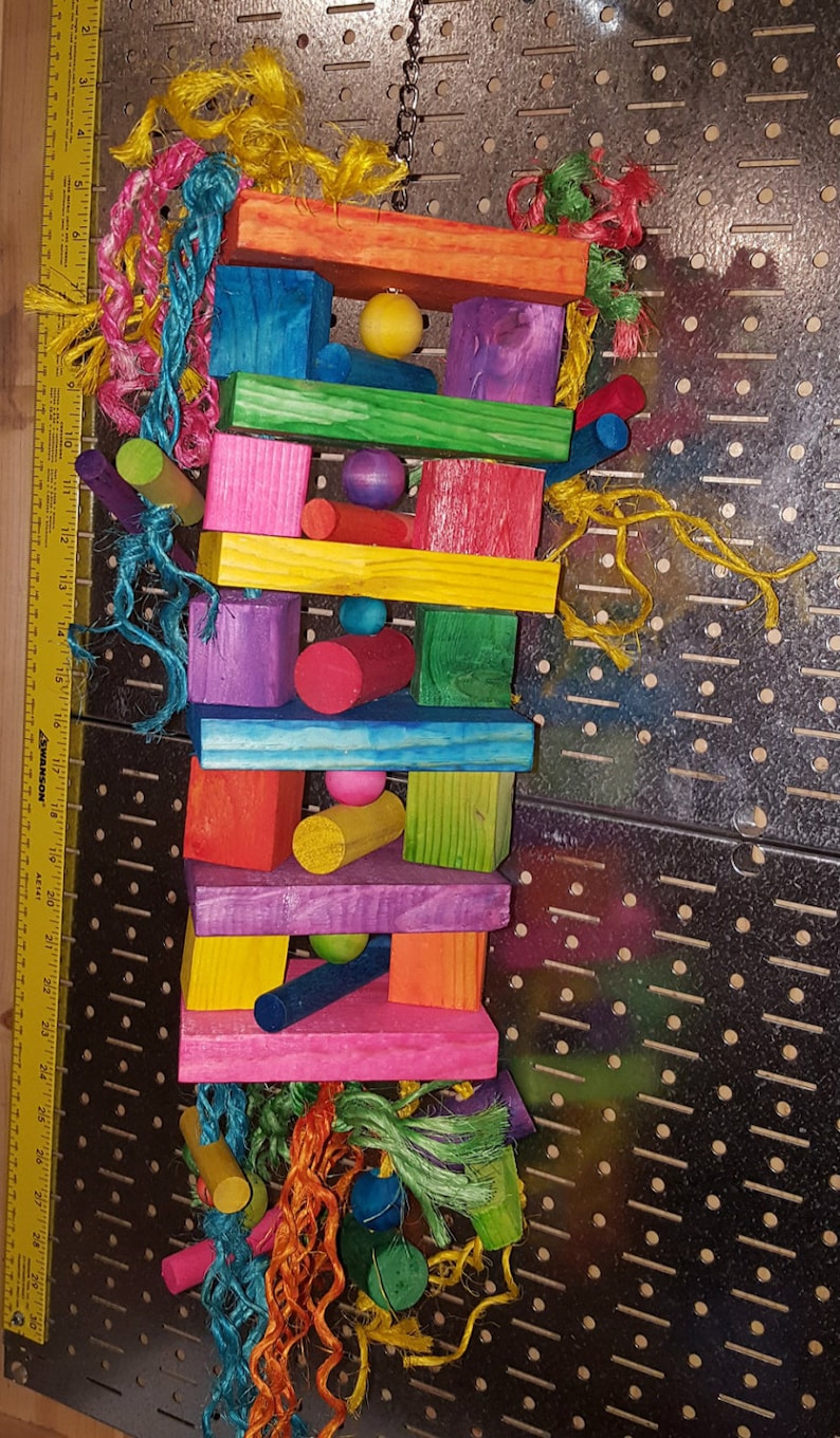 May include: A colorful wooden bird toy with a chain for hanging. The toy is made of various colored wooden blocks, some round, some square, and some rectangular. The toy also has colorful ropes and beads.