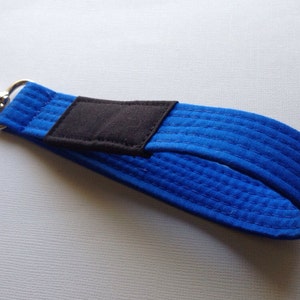 May include: A blue martial arts belt keychain with a black patch and a silver clip.