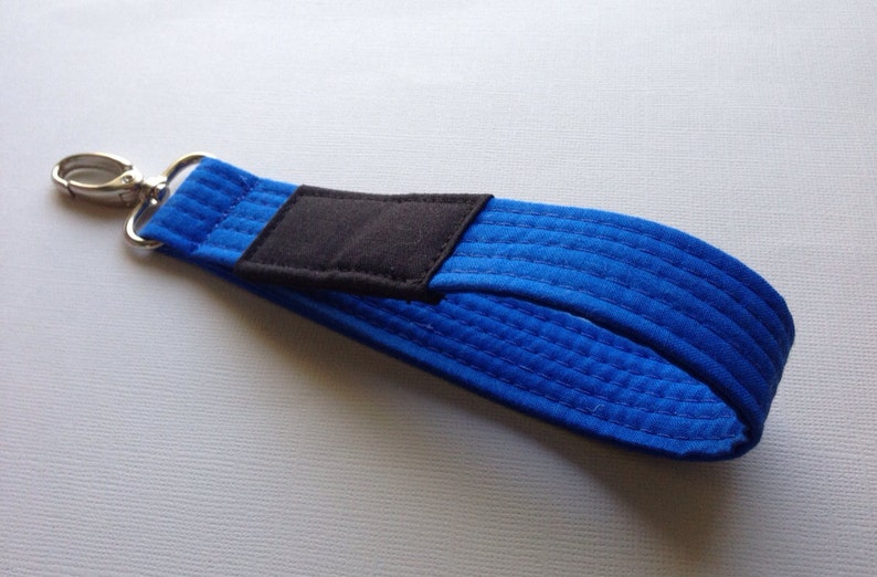 May include: A blue martial arts belt keychain with a black patch and a silver clip.
