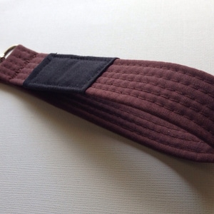 May include: A brown quilted key chain with a black fabric patch and a silver metal hook.