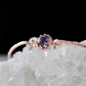 Pode incluir: Um delicado bracelete de ouro rosa com acabamento texturizado e uma &uacute;nica gema roxa engastada em uma moldura em forma de coroa.