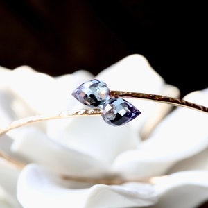 May include: A gold bangle bracelet with two teardrop-shaped amethyst gemstones. The bracelet is hammered and has a delicate, feminine look.