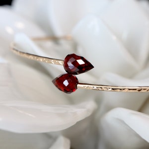 May include: A gold bangle bracelet with two red gemstone accents. The bracelet has a hammered texture.