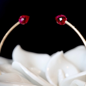 May include: A gold bangle bracelet with two red gemstone accents. The bracelet is photographed against a white background.