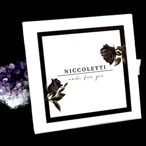 Pode incluir: Caixa branca com borda preta e uma imagem em preto e branco de rosas. O texto "Niccoletti made for you" est&aacute; impresso na caixa.
