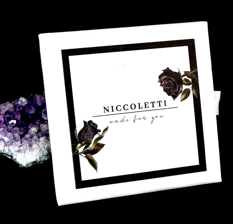 Pode incluir: Caixa branca com borda preta e uma imagem em preto e branco de rosas. O texto "Niccoletti made for you" est&aacute; impresso na caixa.