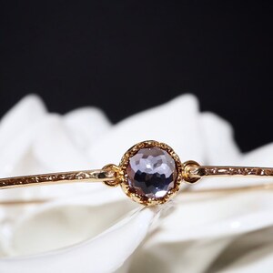 Pode incluir: Um bracelete de ouro com textura martelada e uma &uacute;nica pedra preciosa redonda, facetada, de cor p&uacute;rpura em uma configura&ccedil;&atilde;o de ouro.