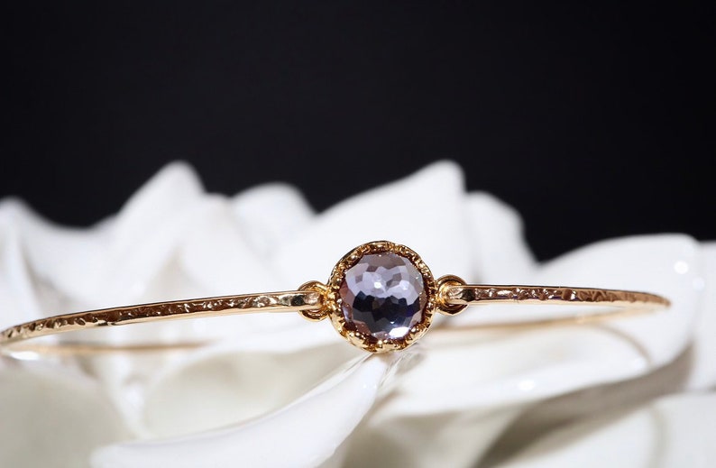 Pode incluir: Um bracelete de ouro com textura martelada e uma &uacute;nica pedra preciosa redonda, facetada, de cor p&uacute;rpura em uma configura&ccedil;&atilde;o de ouro.