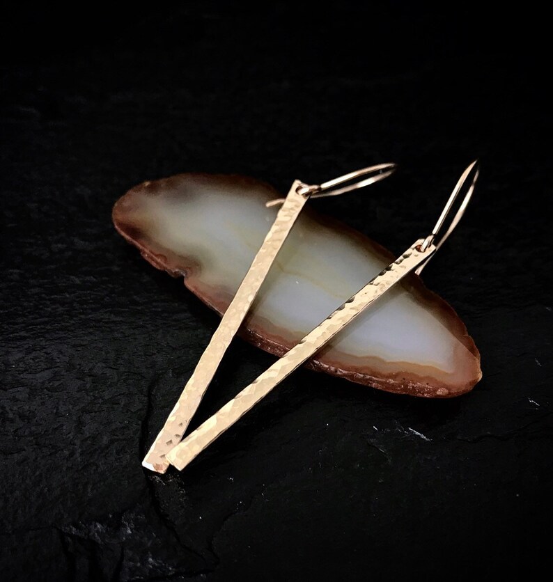 May include: A pair of gold hammered bar earrings with a simple hook closure.