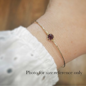 Pode incluir: Um bracelete de ouro com uma &uacute;nica pedra preciosa vermelha engastada em uma moldura de ouro. O bracelete est&aacute; no pulso de uma pessoa. Foto apenas para refer&ecirc;ncia de tamanho.