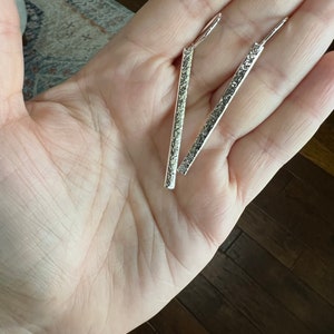 May include: A pair of silver dangle earrings with a textured finish. The earrings are long and straight.