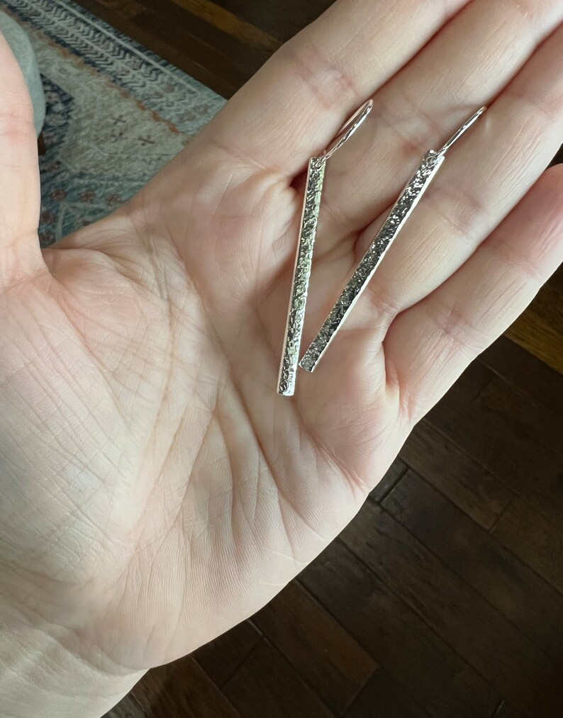 May include: A pair of silver dangle earrings with a textured finish. The earrings are long and straight.
