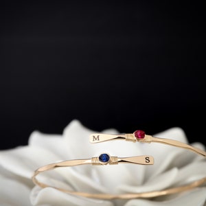 May include: Two gold bracelets with a blue and red gemstone, each engraved with the letter "M" and "S".