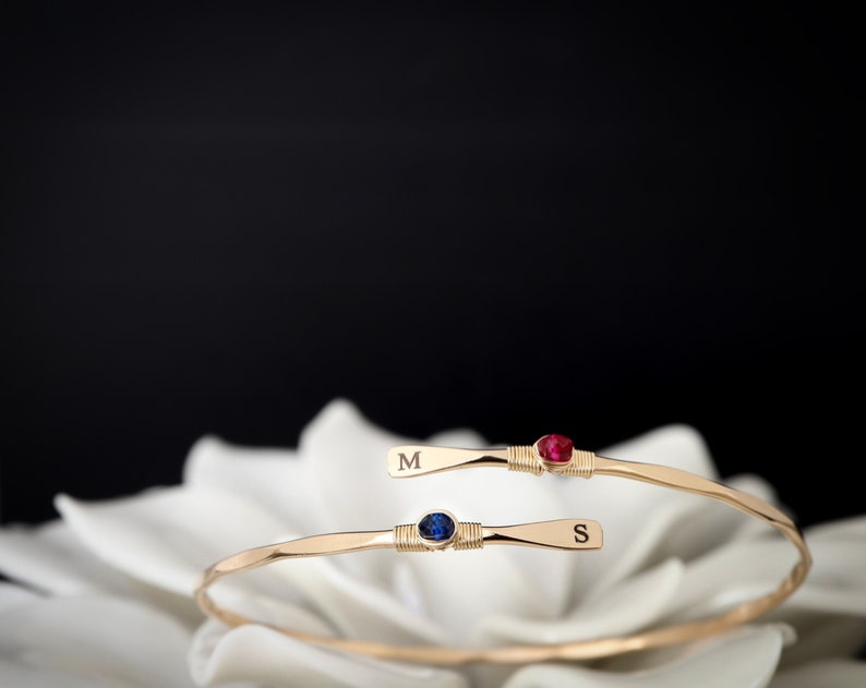 May include: Two gold bracelets with a blue and red gemstone, each engraved with the letter "M" and "S".