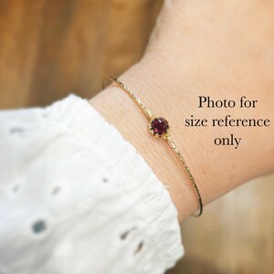 Puede incluir: Un brazalete dorado con una superficie texturizada y una gema roja redonda. El brazalete se muestra en una mu&ntilde;eca, con el texto "Photo for size reference only" visible.