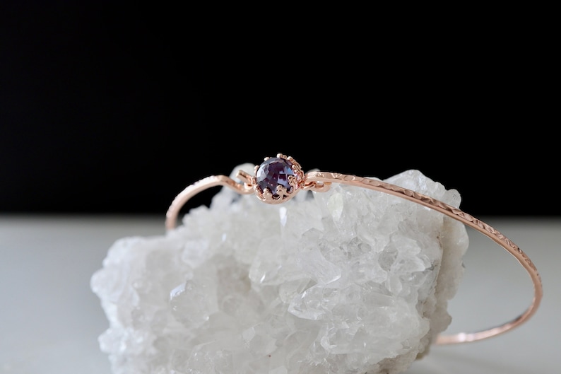 Pode incluir: Um delicado bracelete de ouro rosa com acabamento texturizado e uma &uacute;nica gema roxa engastada em uma moldura em forma de coroa.