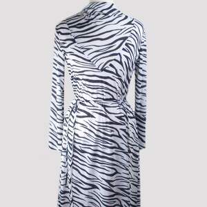 May include: A white and black zebra print midi dress with long sleeves and a tie waist.