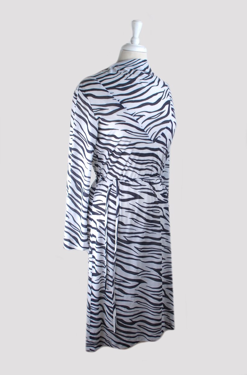 May include: A white and black zebra print long-sleeved dress with a tie at the waist.