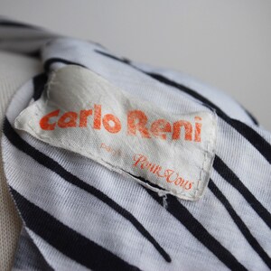 May include: Close-up of a white and black striped shirt with a white label that says "Carlo Reni" in orange lettering and "Pour Vous" in black lettering.