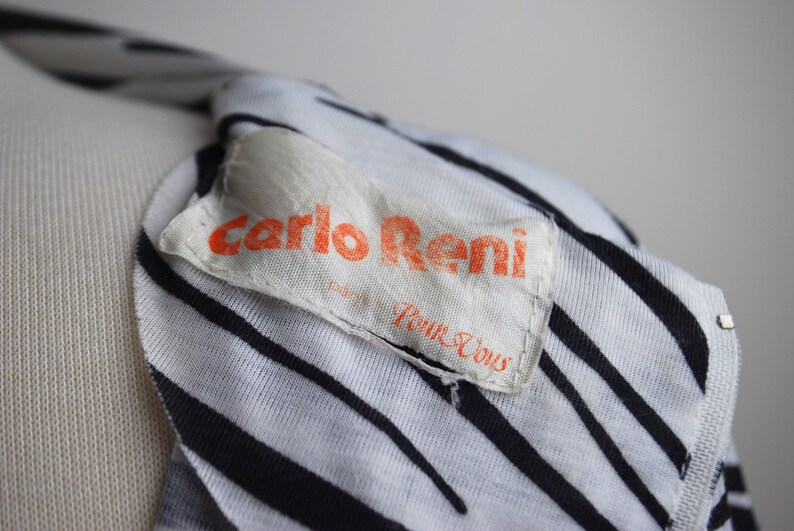 May include: Close-up of a white and black striped shirt with a white label that says "Carlo Reni" in orange lettering and "Pour Vous" in black lettering.