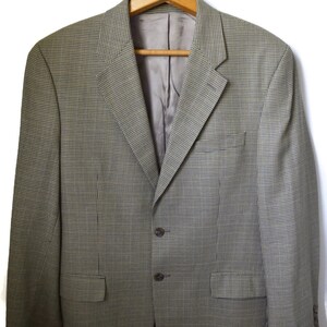 May include: A blazer featuring a fine green and brown micro-check pattern. The garment includes a notched lapel, two dark brown buttons for closure, a single chest pocket, two flap pockets at the waist, and a smooth, solid-colored interior lining.