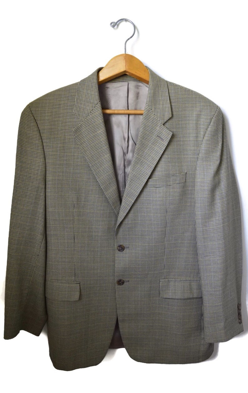 May include: A blazer featuring a fine green and brown micro-check pattern. The garment includes a notched lapel, two dark brown buttons for closure, a single chest pocket, two flap pockets at the waist, and a smooth, solid-colored interior lining.