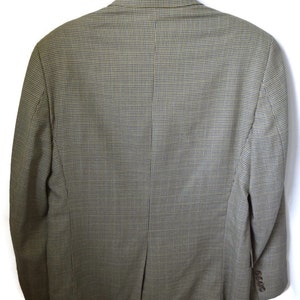 May include: A blazer featuring a fine-scale houndstooth pattern in shades of olive green and brown. The garment is displayed from the back, showing a center vent, long sleeves with four buttons on each cuff, and a structured collar on a hanger.