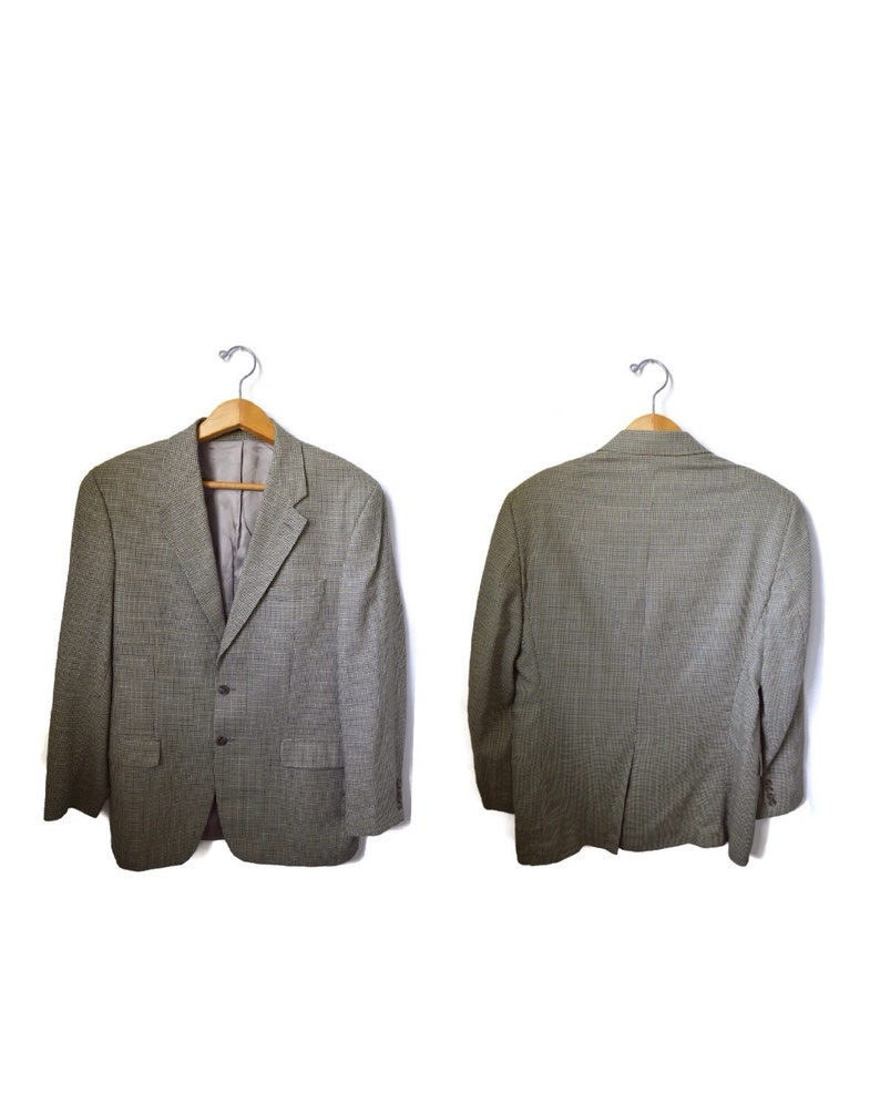 May include: A gray and black micro-check blazer featuring a notched lapel, two front buttons, two flap pockets, and long sleeves. The garment is displayed on a wooden hanger, showing both the front view with a gray lining and the back view.