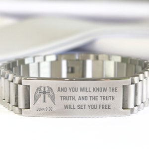 May include: A silver bracelet with a stainless steel band and a rectangular charm engraved with the words "AND YOU WILL KNOW THE TRUTH, AND THE TRUTH WILL SET YOU FREE" and "JOHN 8:32". The charm also features a stylized image of a winged cross.