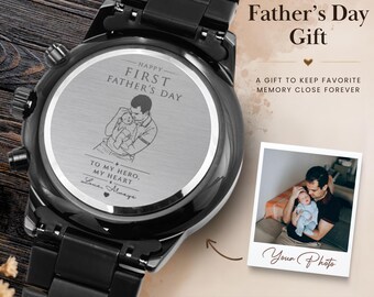 Può includere: Un orologio da polso in metallo nero con un fondello circolare in argento inciso con un'illustrazione a linee di una persona che tiene in braccio un bambino, il testo "HAPPY FIRST FATHER'S DAY" e "TO MY HERO, MY HEART", con una foto.