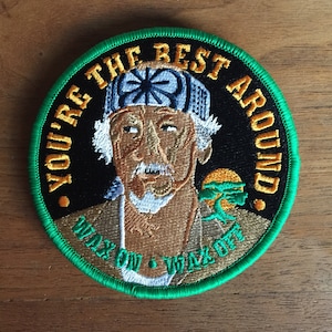 May include: A green and yellow embroidered patch featuring a cartoon image of Mr. Miyagi from the movie 'The Karate Kid'. The patch has the text 'You're the best around' and 'Wax on, Wax off' in a yellow font.