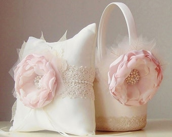 May include: A white satin pillow with a pink flower and lace trim, and a white basket with a pink flower and lace trim. Both items are for a wedding ceremony.