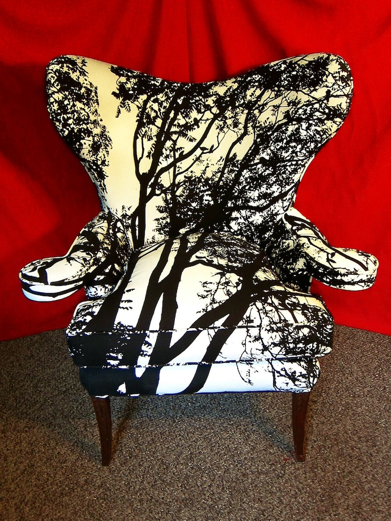 May include: A black and white patterned armchair with a silhouette of trees. The chair has a high back and wing arms. The chair is sitting on a red carpet.