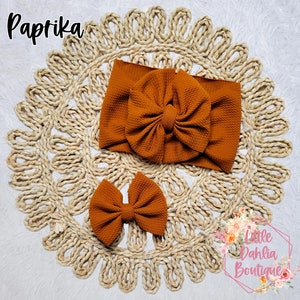 May include: A set of two brown fabric headbands with a large bow. The headband is made of a soft, stretchy fabric and is perfect for adding a touch of style to any outfit. The headband is available in a variety of colors.